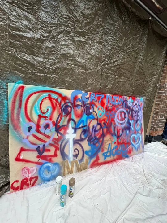 A spray-painted board in red, blue and purple, with spray cans in front